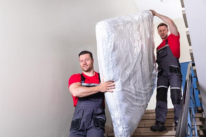 two workers carrying a heavy box spring out of a bedroom in Battle Creek MI